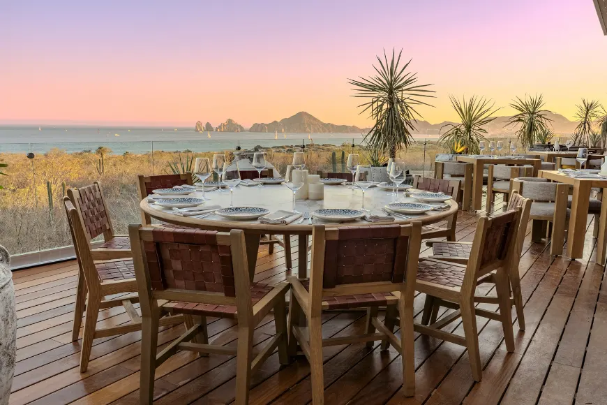 A terrace restaurant table set for dinner at dusk, overlooking the bay and Land's End in Los Cabos.